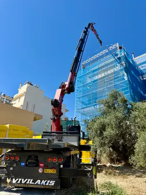 Γερανός σε εργασία δίπλα σε κτήριο καλυμμένο με προστατευτικά δίχτυα σκαλωσιάς