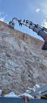 Βραχίονας γερανού σε εργασία μπροστά από βραχώδες πρανές με δέματα υλικών